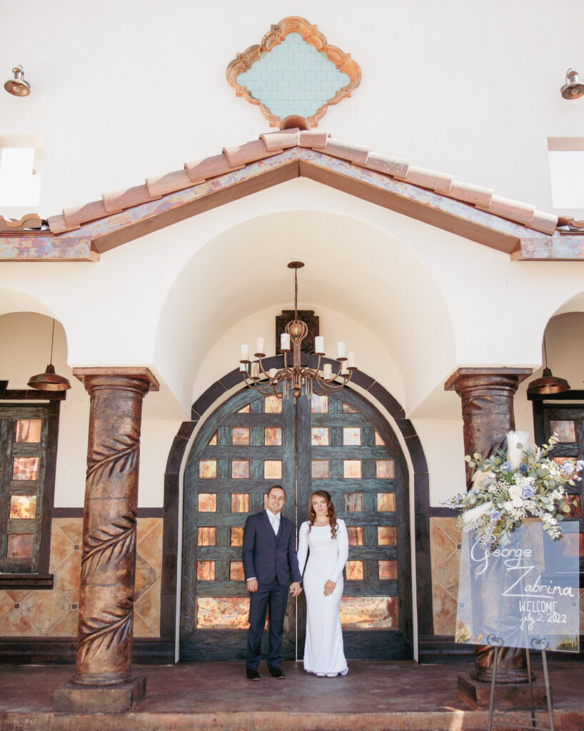 young newly wed couple stands outside of the front doors of the Spanish hacienda 